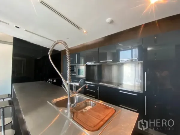 公寓 出租在Sathon, Bangkok - 现代厨房，不锈钢中岛配弹簧龙头，黑色亮面橱柜与嵌入式家电。