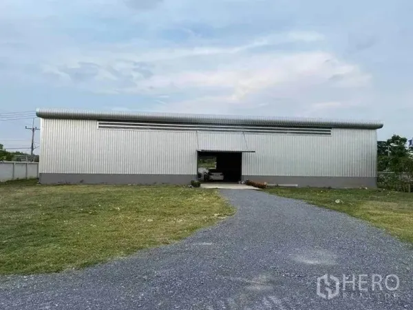 Warehouse for rent in Sam Phran, Nakhon Pathom - Front exterior of corrugated metal warehouse with wide driveway and large grassed yard.