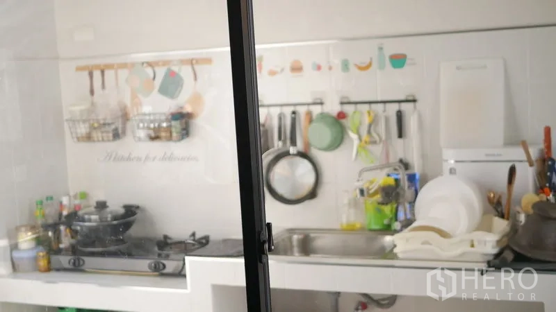 Detached House for rent or sale in Bang Bo, Samut Prakan - Separate Thai kitchen with gas cooktop, stainless sink and utensil rack behind glass.