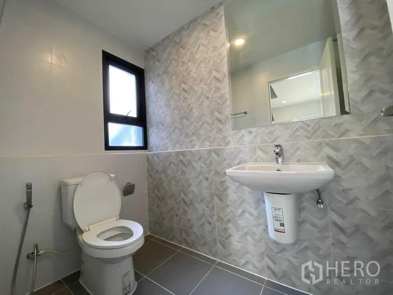 Detached House for rent in Don Mueang, Bangkok - Bathroom with toilet, patterned wall tiles, pedestal sink and window.
