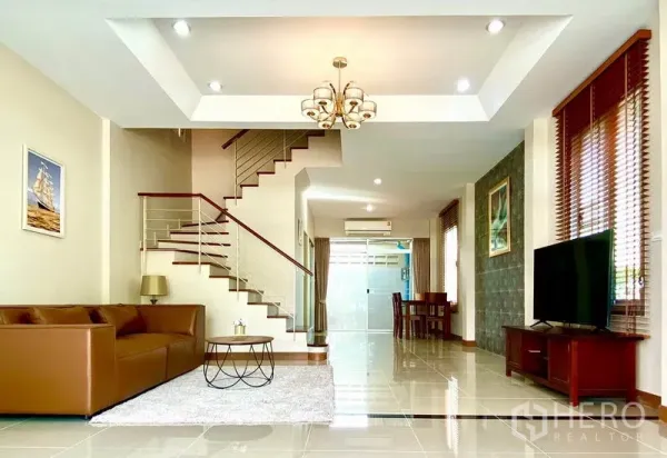 ทาวน์เฮาส์ ให้เช่าในPrawet, Bangkok - ห้องนั่งเล่นโปร่งสว่าง เพดานหลุม โคมไฟ ทีวี และบันไดเชื่อมชั้น พร้อมหน้าต่างบานใหญ่.