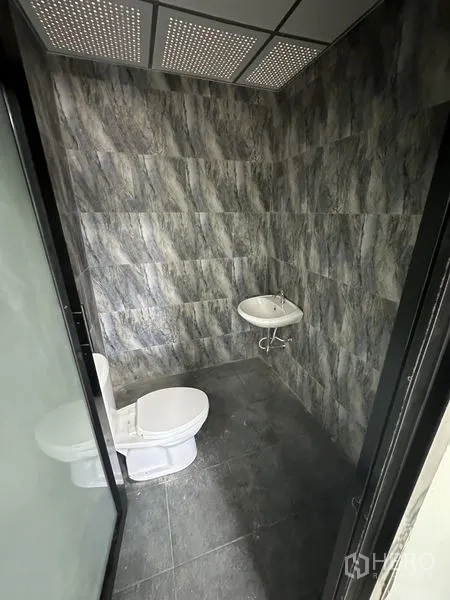 Factory for rent in Chachoengsao - Restroom with gray stone‑effect wall tiles, toilet and wall‑mounted sink.