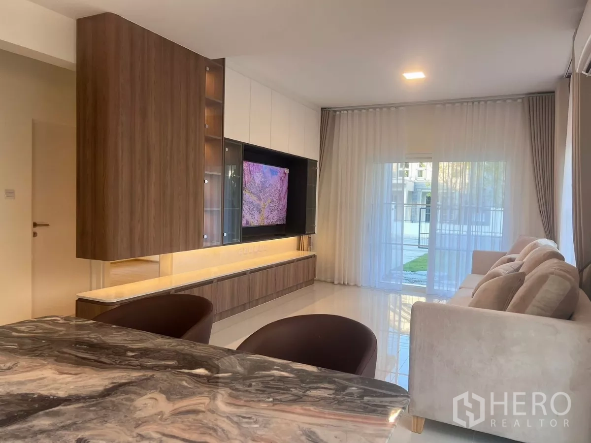 Detached House for rent in Bang Phli, Samut Prakan - Dining area with marble table, TV feature wall and sliding glass doors to the garden.