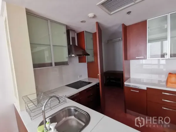 Condominium for rent in Pathum Wan, Bangkok - Compact kitchen with cooktop, range hood, and stainless sink beside pantry cabinets.
