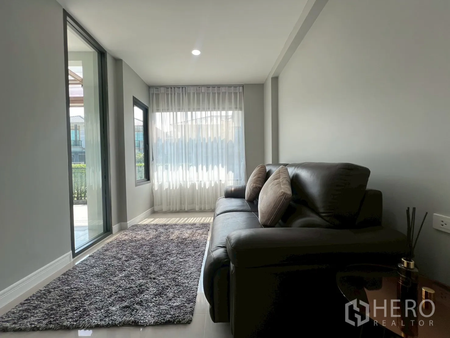 Detached House for rent or sale in Bang Phli, Samut Prakan - Cozy sitting area with black leather sofa, rug and sliding glass door to terrace.
