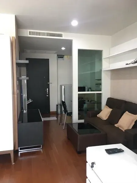 คอนโด ให้เช่าในPathum Wan, Bangkok - โถงทางเข้าพร้อมพื้นที่นั่งเล่นแบบโอเพนแปลน ชั้นวางบิวท์อิน โซฟาสีน้ำตาล และพื้นไม้