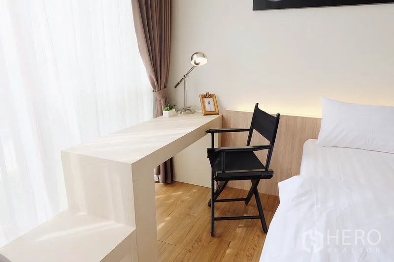 Condominium for sale in Watthana, Bangkok - Work corner with white desk and black chair beside tall windows and brown drapes.