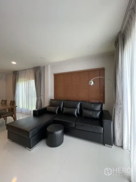 Detached House for rent in Bang Phli, Samut Prakan - Close view of L-shaped black leather sofa by window with blinds and a floor lamp.
