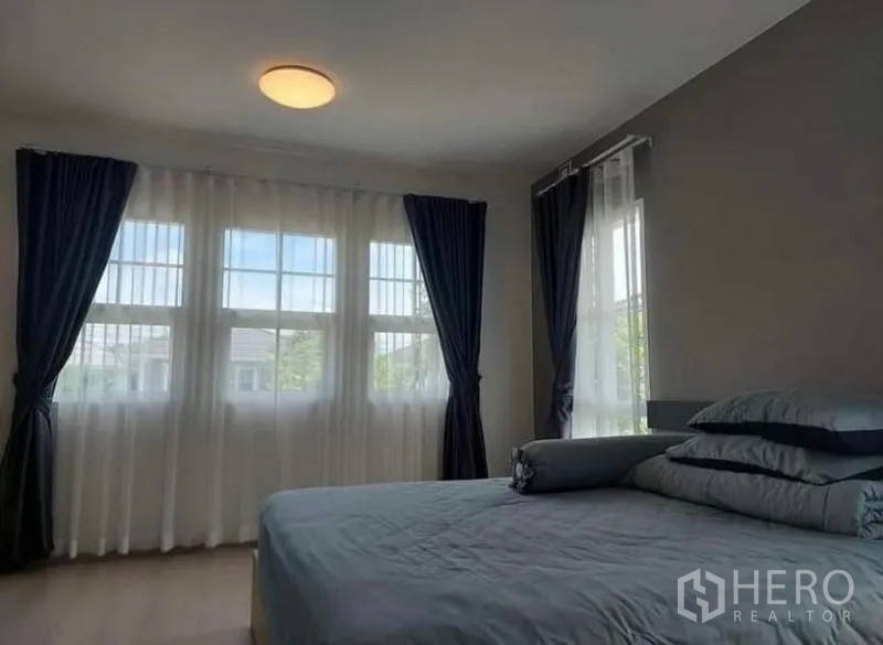 Detached House for rent in Bang Bo, Samut Prakan - Spacious bedroom with multiple windows, soft natural light and dark curtains.