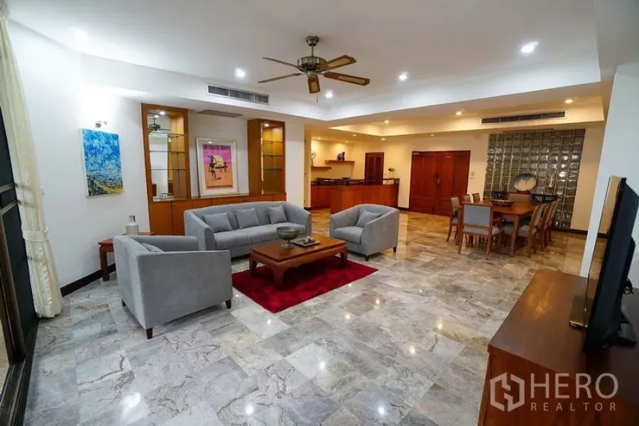 อพาร์ทเมนท์ ให้เช่าในWatthana, Bangkok - ห้องนั่งเล่นกว้างด้วยชุดโซฟาสีเทา พัดลมเพดาน และผนังกระจกบล็อกใกล้โซนรับประทานอาหาร.