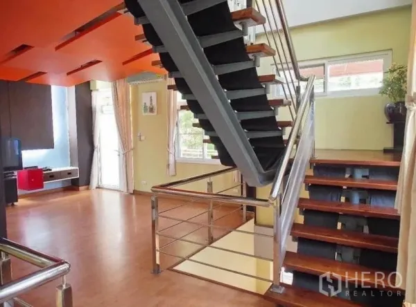 Townhouse for rent in Wang Thonglang, Bangkok - Open-plan living area featuring an industrial metal staircase, orange ceiling panels and wide windows.