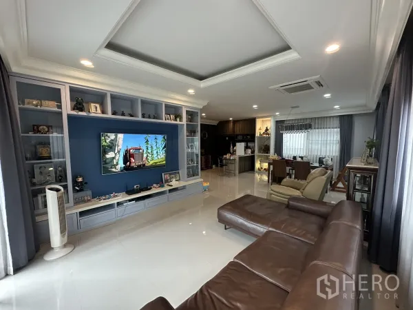 บ้าน ให้เช่าในLam Luk Ka, Pathum Thani - ห้องรับแขกสว่าง ผนังตู้สื่อสีน้ำเงิน ฝ้าหลุม และต่อเนื่องสู่ส่วนทานอาหาร