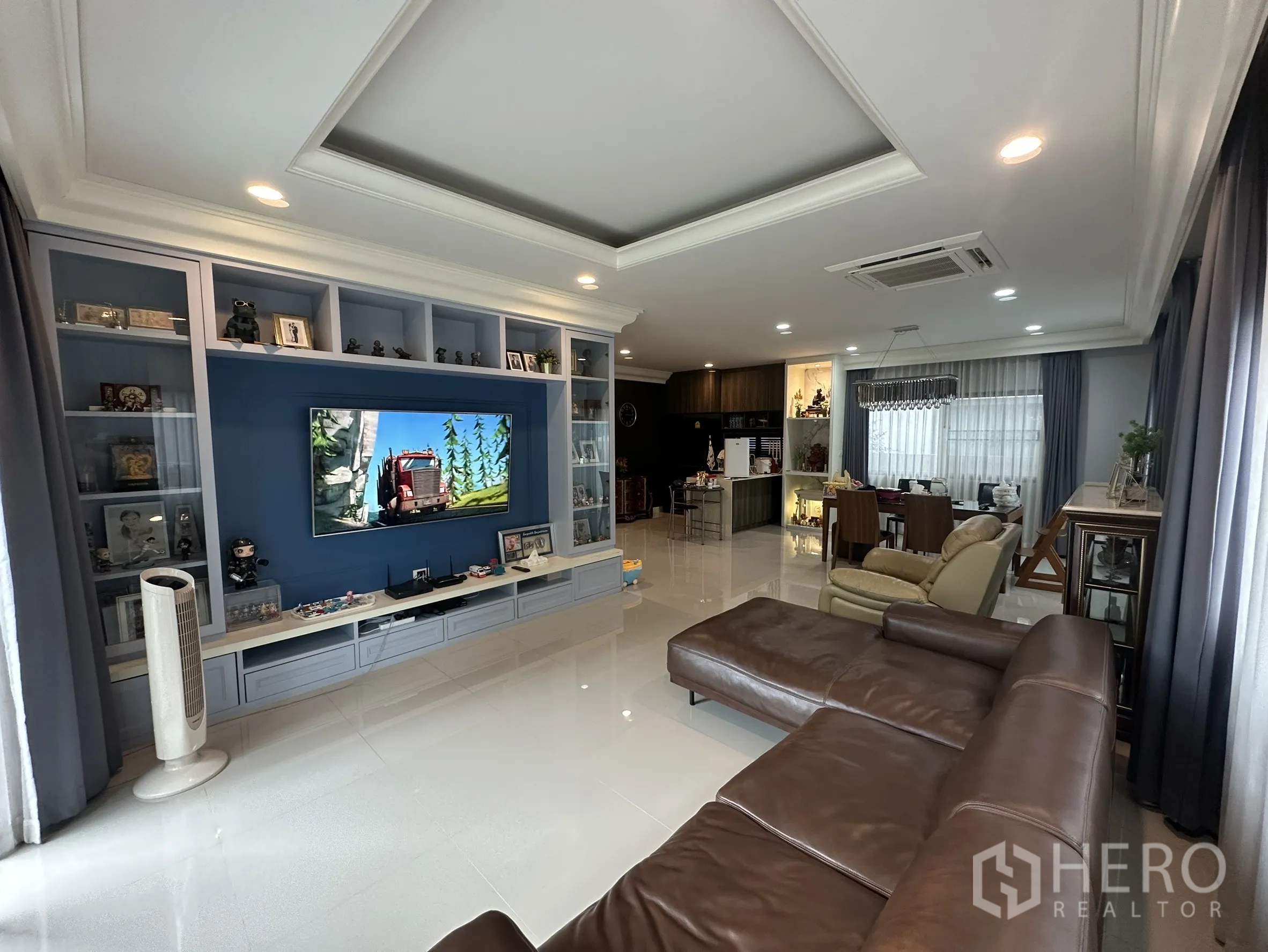 บ้าน ให้เช่าในLam Luk Ka, Pathum Thani - ห้องรับแขกสว่าง ผนังตู้สื่อสีน้ำเงิน ฝ้าหลุม และต่อเนื่องสู่ส่วนทานอาหาร