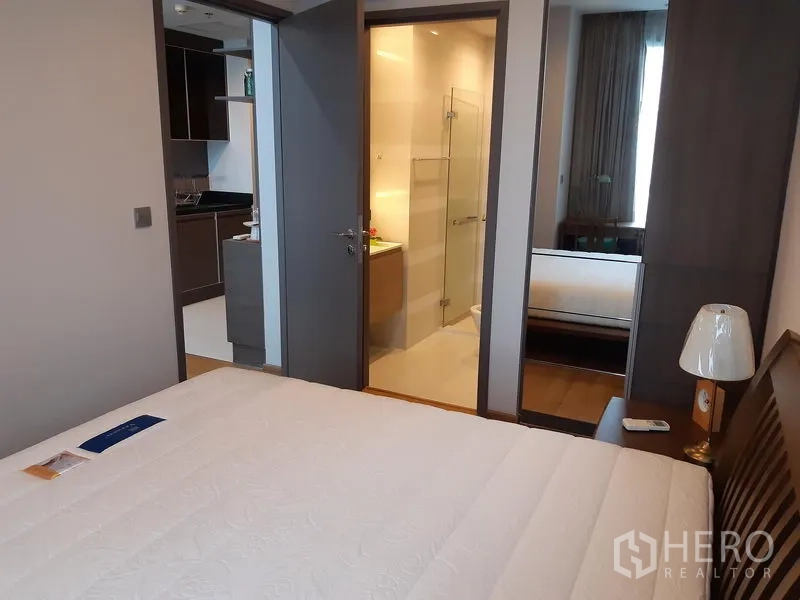 คอนโด ให้เช่าในKhlong Toei, Bangkok - ห้องนอนอบอุ่น เตียงขนาดใหญ่ โคมไฟข้างเตียง ตู้เสื้อผ้าบานกระจก และประตูเข้าสู่ห้องน้ำ