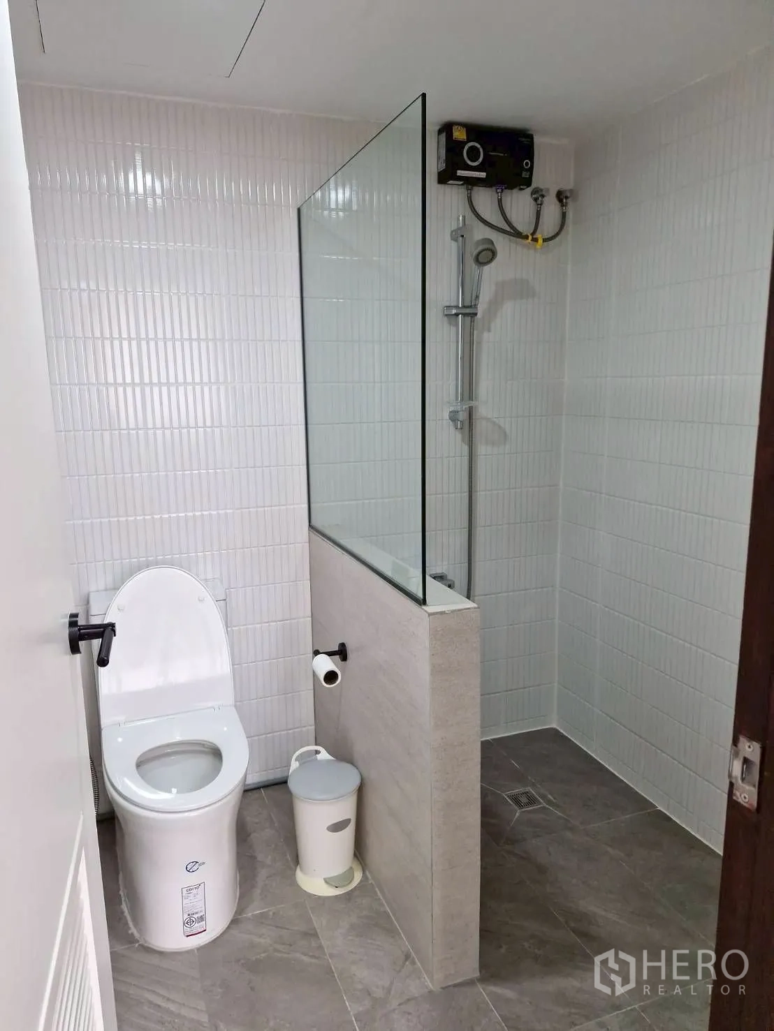 Condominium for rent in Khlong Toei, Bangkok - Modern bathroom with glass-partition walk-in shower, white toilet and tiled walls.