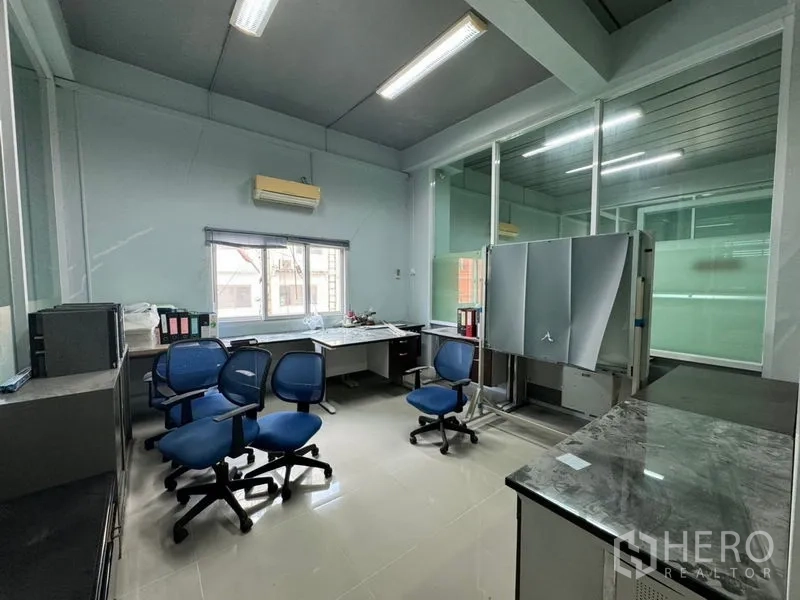 Warehouse for rent or sale in Chon Buri - Private office with desks, blue chairs and a window-mounted air conditioner.