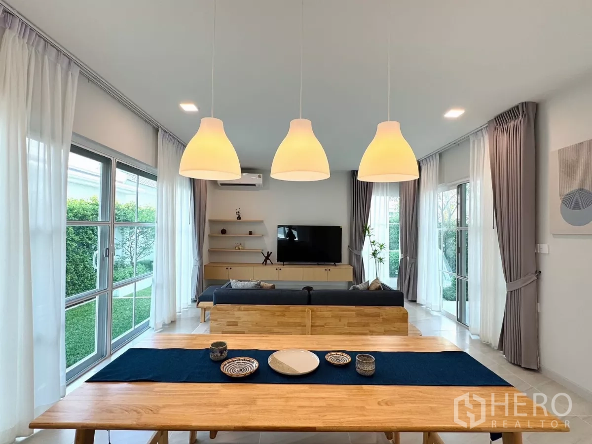 Detached House for rent in Bang Phli, Samut Prakan - Pendant lights over a wooden dining table facing the garden and living zone.