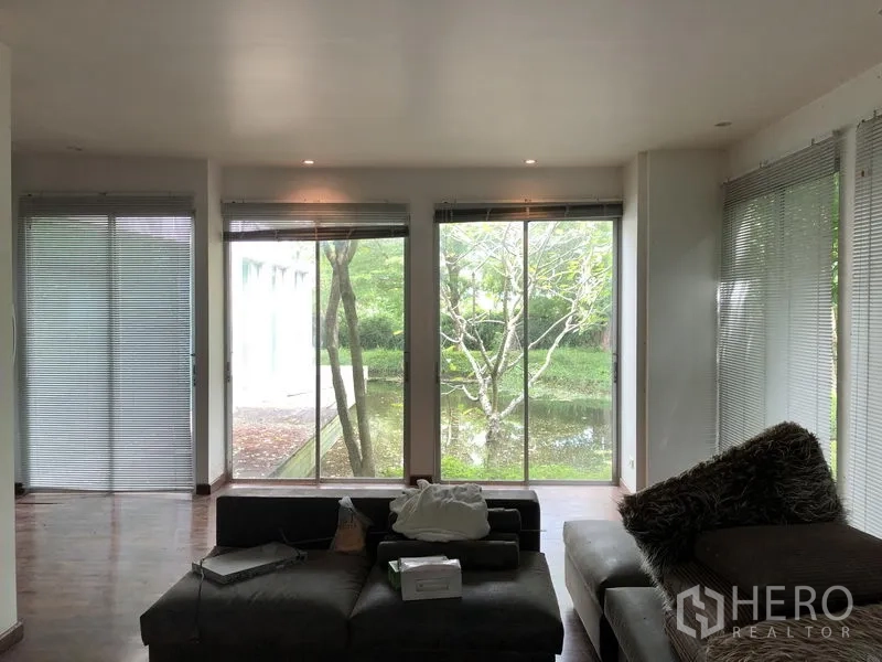 Factory for rent in Pathum Thani - Living area with floor-to-ceiling windows overlooking a reflective pond and trees.