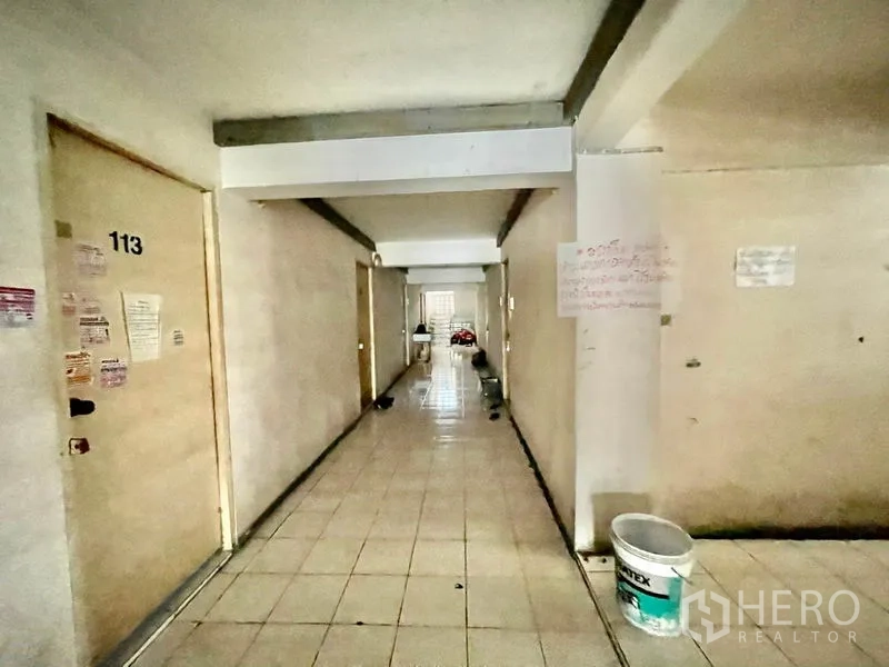 Apartment for sale in Mueang Samut Prakan, Samut Prakan - Lower-floor corridor with numbered doors and tiled floors.