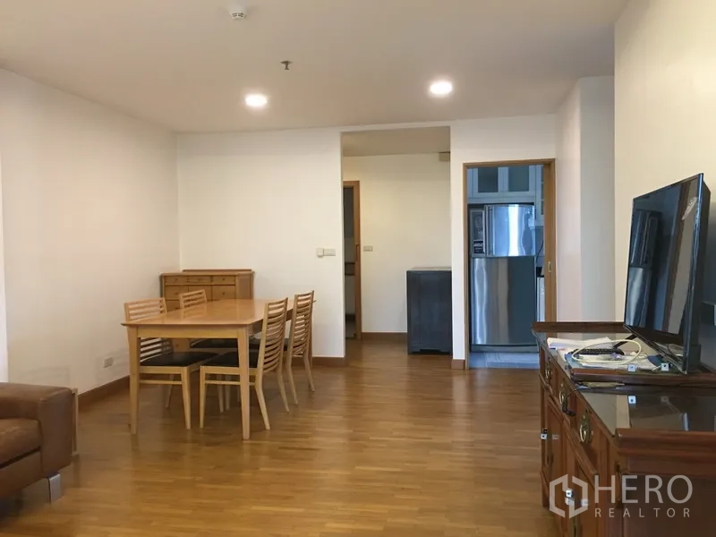Condominium for rent in Pathum Wan, Bangkok - Dining area with six-seat wooden table beside living zone and TV, doorway to the kitchen.