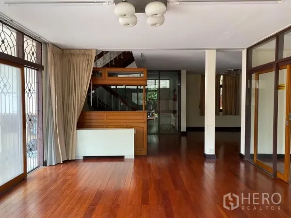 บ้าน ให้เช่าในKhlong Toei, Bangkok - ห้องนั่งเล่นสว่างพื้นไม้จริงขัดเงา หน้าต่างบานใหญ่มีเหล็กดัด และบันไดขึ้นชั้นบน