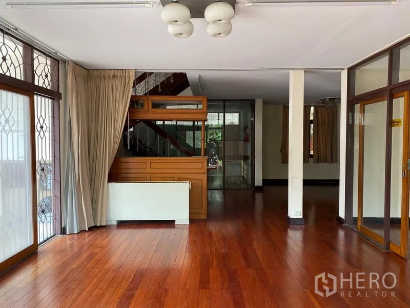 บ้าน ให้เช่าในKhlong Toei, Bangkok - ห้องนั่งเล่นสว่างพื้นไม้จริงขัดเงา หน้าต่างบานใหญ่มีเหล็กดัด และบันไดขึ้นชั้นบน