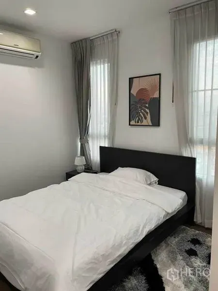 Condominium for rent or sale in Watthana, Bangkok - Bright bedroom with AC, two tall windows, grey curtains and a framed art above a dark bed.