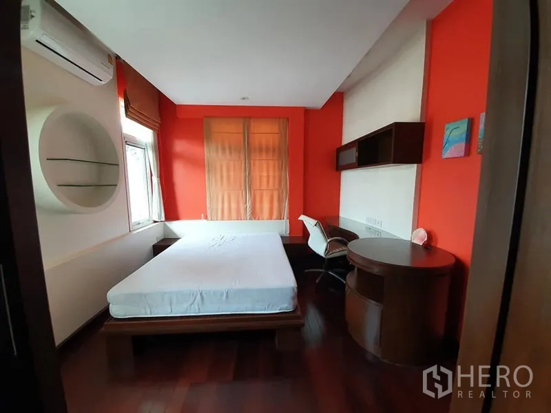 Detached House for rent in Wang Thonglang, Bangkok - Bedroom with orange accent wall, built-in desk and shelves, air-conditioning and wood floors.