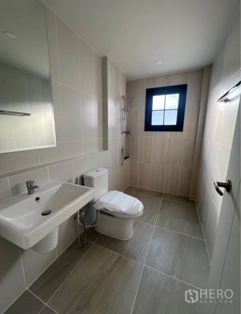 Detached House for rent in Bang Phli, Samut Prakan - Bright bathroom with beige tiles, walk-in shower, sink, toilet and a window.