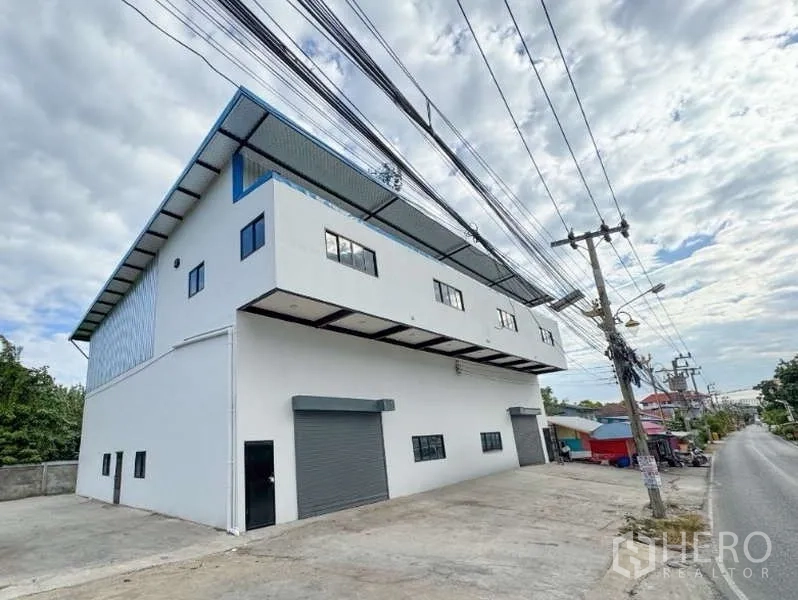 คลังสินค้า ให้เช่าในBang Phli, Samut Prakan - อาคารโกดังสองชั้นสมัยใหม่ ผนังสีขาว มีประตูม้วนสองจุดและลานคอนกรีตกว้างติดถนนสงบในบางพลี