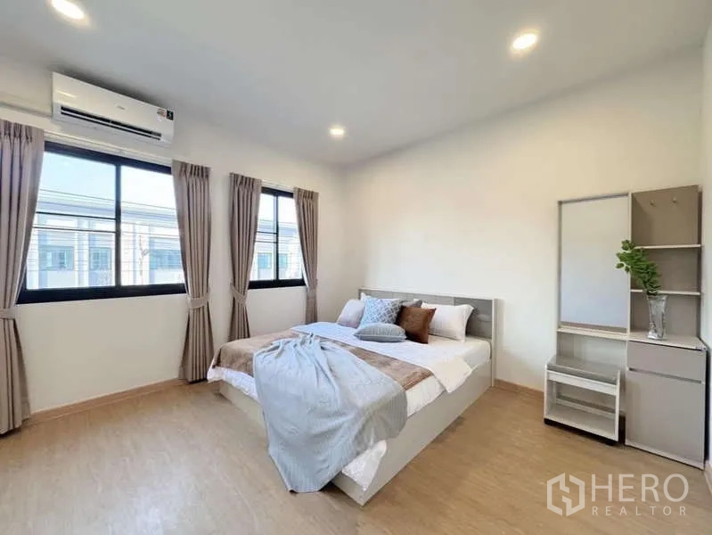 Townhouse for rent in Min Buri, Bangkok - Spacious master bedroom with corner windows, bed and compact dressing unit.
