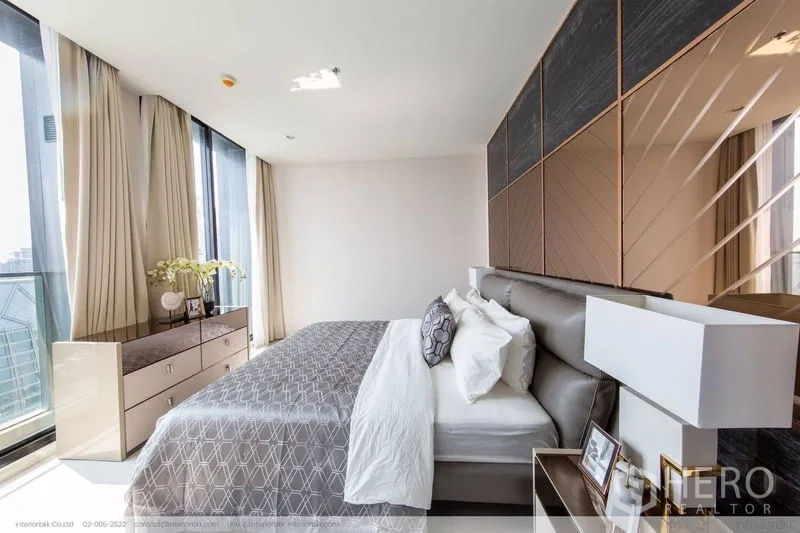 Condominium for rent in Pathum Wan, Bangkok - Bedroom angle showing dresser by large windows with skyline views and soft curtains.