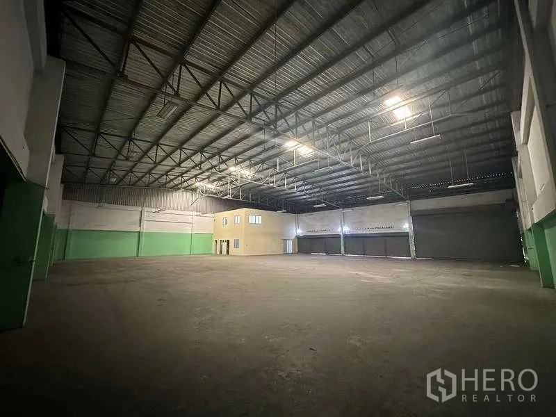 工厂 出租在Nonthaburi - 高净空仓库内部，沿墙分布多道装卸卷帘门与通透空间。