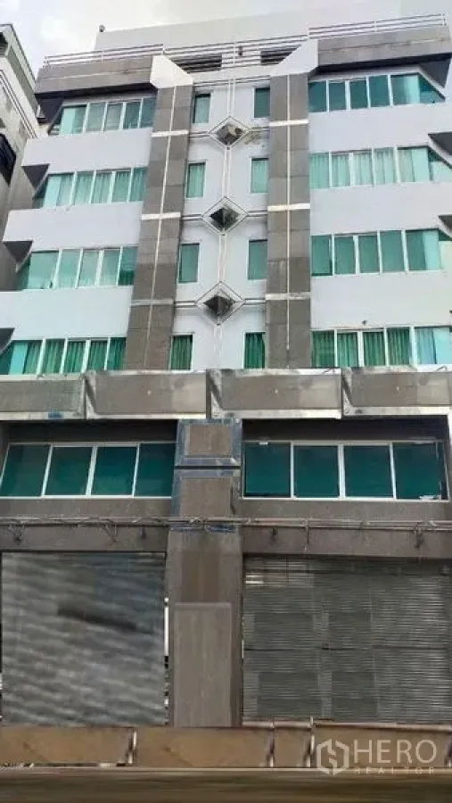 สำนักงาน ให้เช่าในPrawet, Bangkok - ด้านหน้าตึกสำนักงานสูงปานกลาง หน้าต่างกระจกเขียวและประตูม้วนโลหะ ในเขตประเวศ กรุงเทพฯ