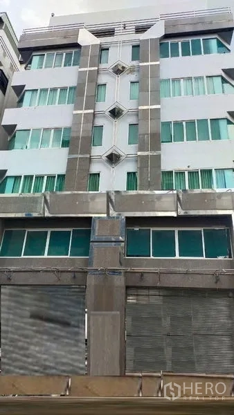 สำนักงาน ให้เช่าในPrawet, Bangkok - ด้านหน้าตึกสำนักงานสูงปานกลาง หน้าต่างกระจกเขียวและประตูม้วนโลหะ ในเขตประเวศ กรุงเทพฯ