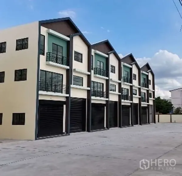 Warehouse for sale in Lat Lum Kaeo, Pathum Thani - Row of modern three-story warehouse units with roller shutters and a wide driveway.