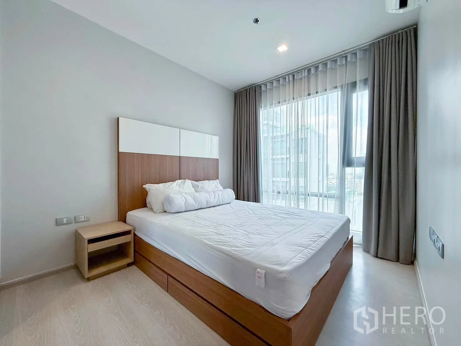 Condominium for rent in Khlong Toei, Bangkok - Bedroom with large window, sheer curtains, and wooden bed frame.