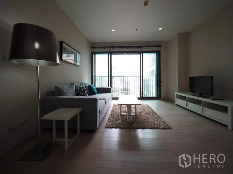 公寓 出租在Watthana, Bangkok - 客厅配沙发与电视柜，落地窗通向阳台，城市景观尽收眼底。