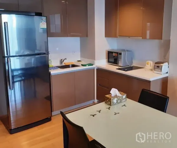 公寓 出租在Khlong Toei, Bangkok - 现代开放式厨房，亮面橱柜、不锈钢冰箱、内置电炉与微波炉，配玻璃餐桌。