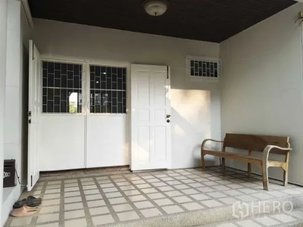Townhouse for rent or sale in Suan Luang, Bangkok - Covered front porch with white entry door, tiled floor and wooden bench.