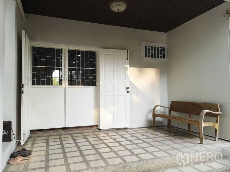 Townhouse for rent or sale in Suan Luang, Bangkok - Covered front porch with white entry door, tiled floor and wooden bench.