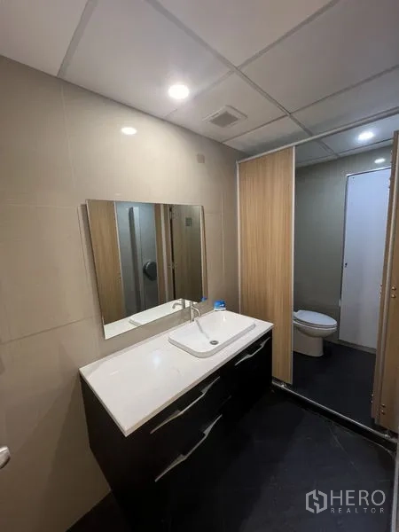 办公空间 出租 - 现代化办公室卫生间，宽大洗手台、镜面与收纳柜，筒灯照明。