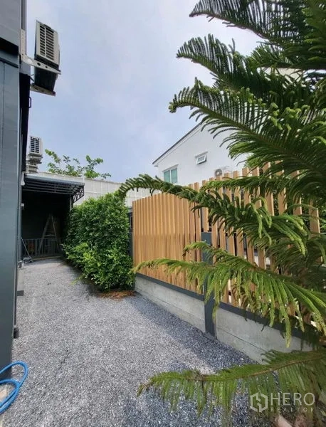 Townhouse for rent or sale - Side yard with gravel path, tall wooden privacy fence and mature greenery along the townhouse.