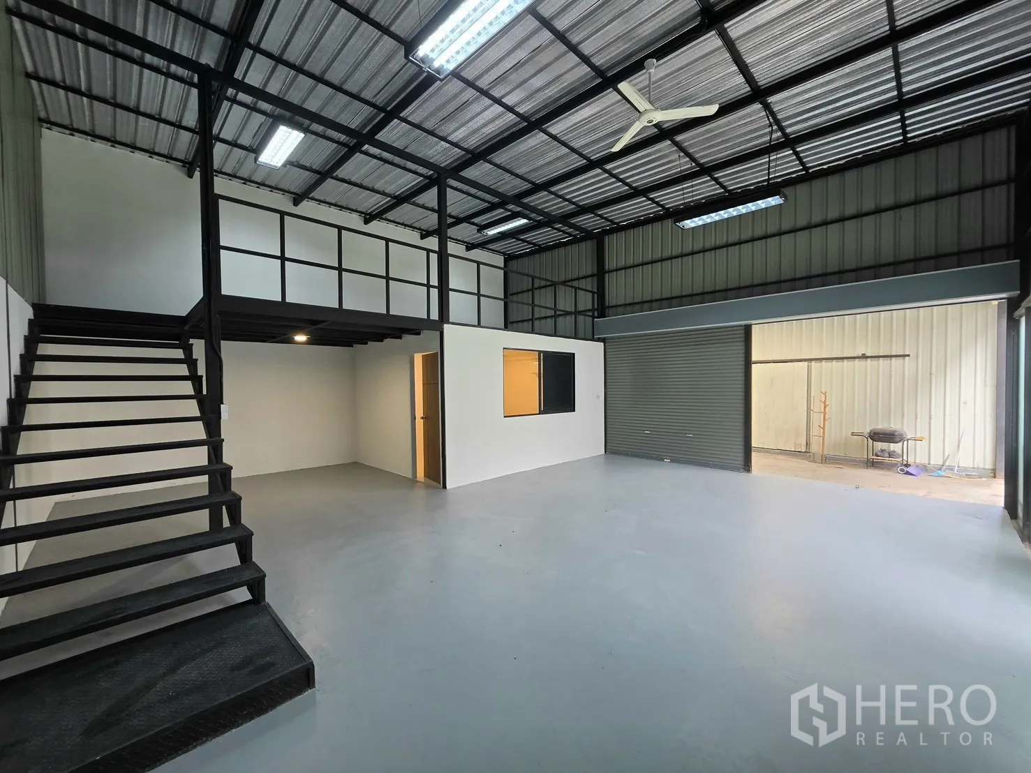 Warehouse for rent in Suan Luang, Bangkok - Spacious warehouse area with mezzanine, stairs, and open roller shutter.