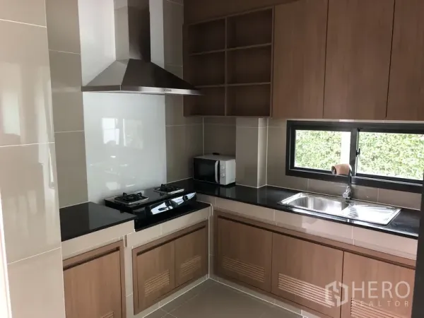 Detached House for rent in Bang Kapi, Bangkok - Modern fitted kitchen with gas hob, stainless hood, black countertops, and wood cabinetry.