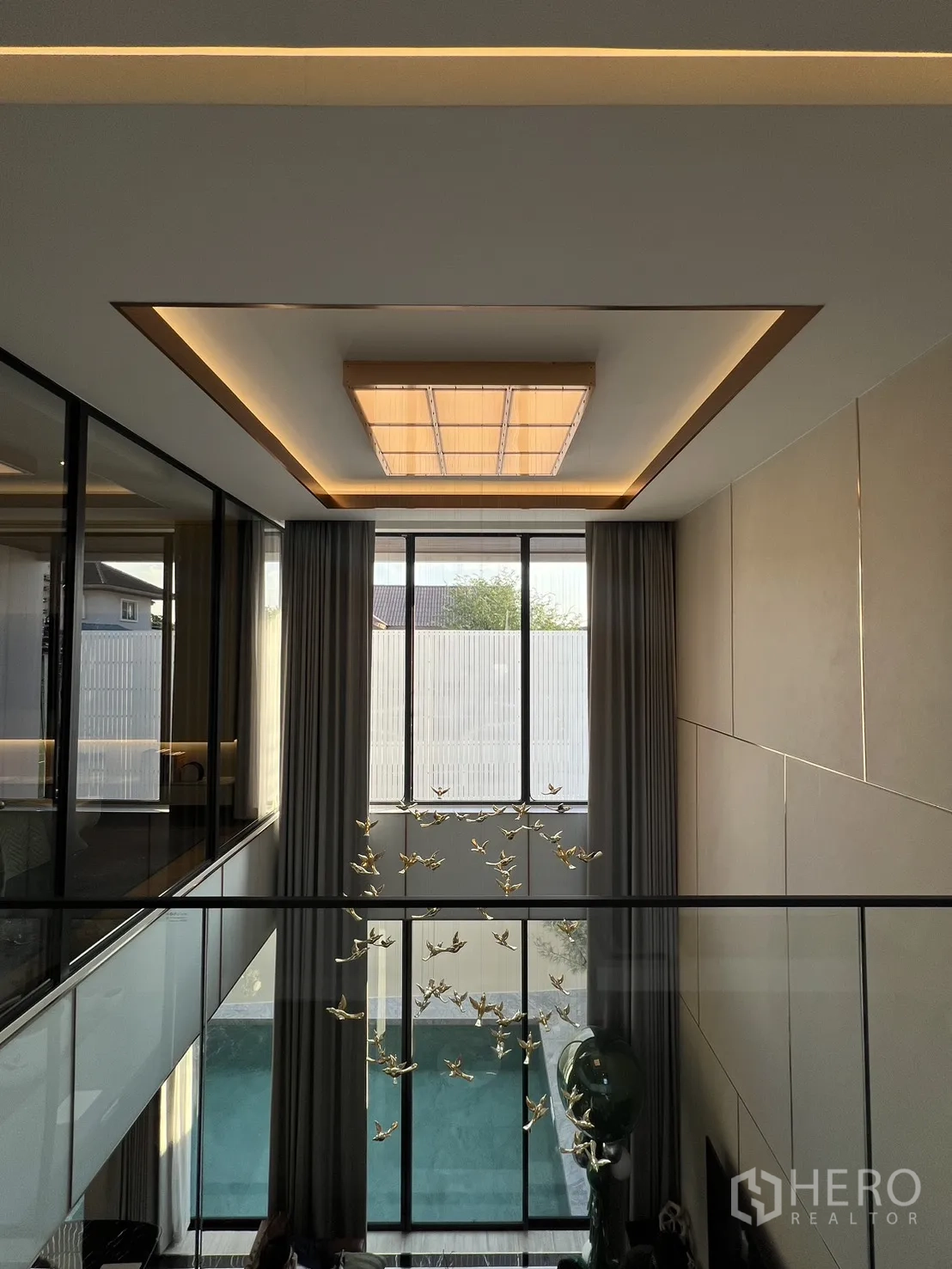 บ้าน ขายในLat Phrao, Bangkok - โถงชั้นลอยมองเห็นห้องนั่งเล่นและสระว่ายน้ำผ่านผนังกระจกสูง