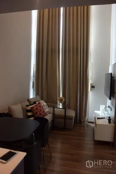 Condominium for rent in Watthana, Bangkok - Living area with high ceilings, floor-to-ceiling curtains and a compact sofa beside the dining table.