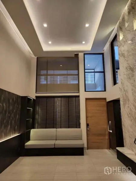 ทาวน์เฮาส์ ขายในYan Nawa, Bangkok - ห้องนั่งเล่นเพดานสูง ไฟซ่อน โซฟา และมู่ลี่โทนเข้ม ในทาวน์เฮาส์สไตล์โมเดิร์น.