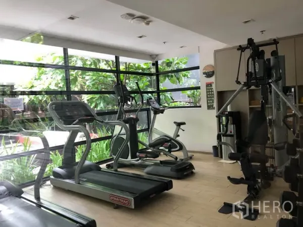 Condominium for rent in Watthana, Bangkok - Fitness room equipped with treadmills, elliptical machines, and a weight station overlooking the garden.