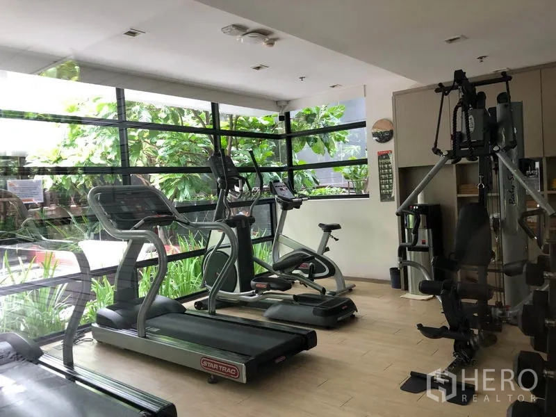Condominium for rent in Watthana, Bangkok - Fitness room equipped with treadmills, elliptical machines, and a weight station overlooking the garden.